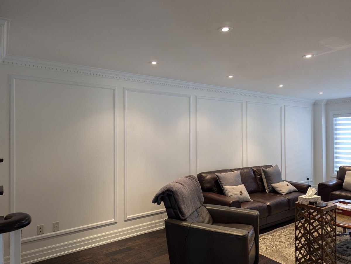 Interior panel moulding in a white living room, tall single-row boxes running the length of the wall under crown moulding