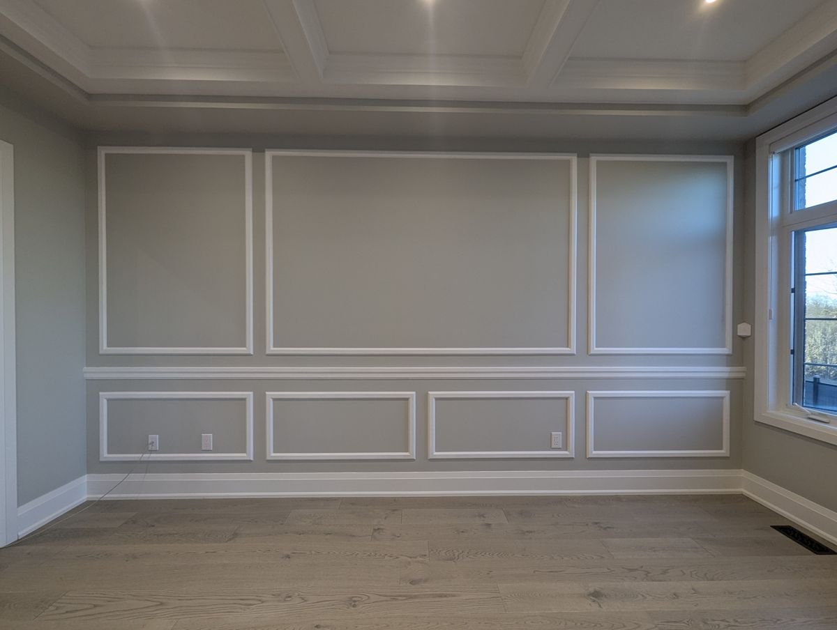 Picture-frame wainscoting in a gray family room, an even run of boxes meeting the door casing